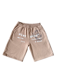 A pair of beige athletic shorts with a gray graphic print on the left leg and white text on the right leg, displayed flat against a white background.
