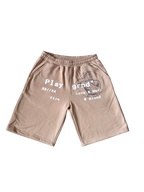 A pair of beige athletic shorts with a gray graphic print on the left leg and white text on the right leg, displayed flat against a white background.
