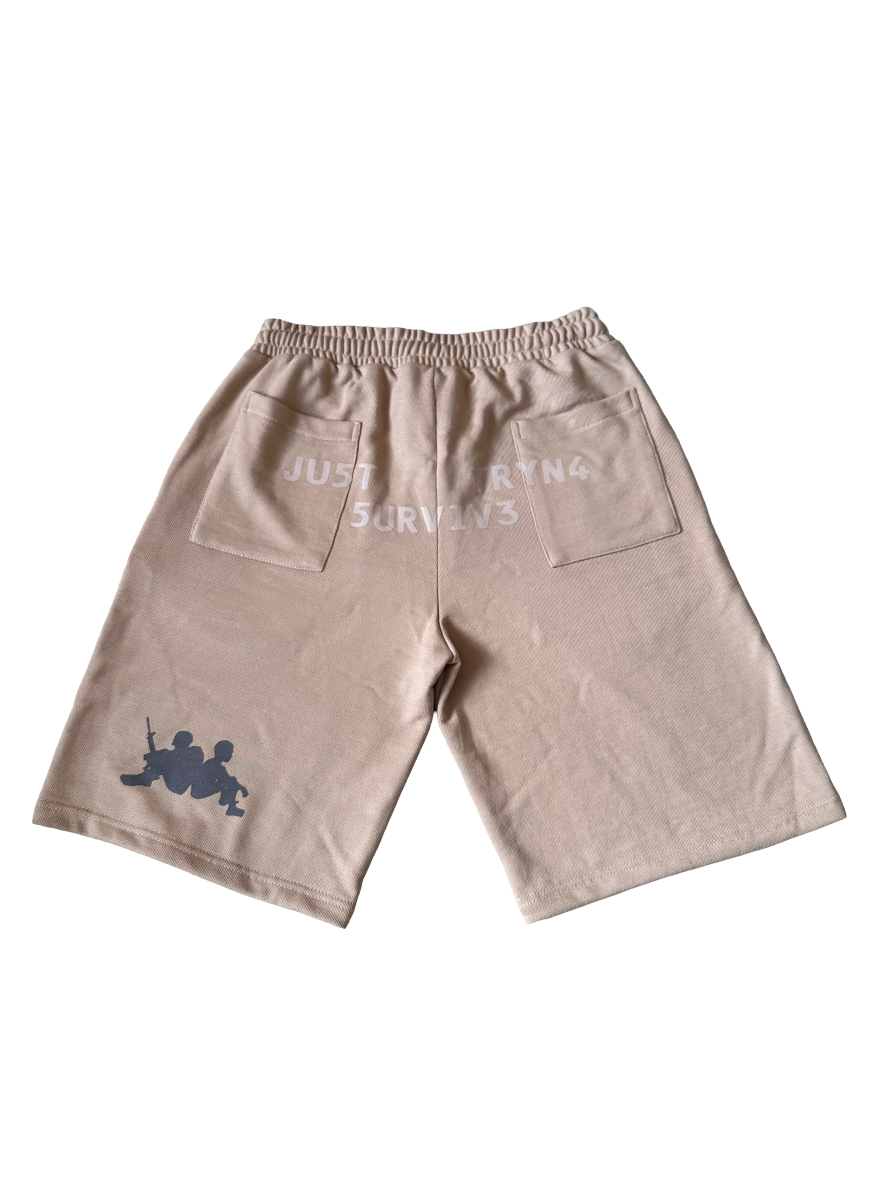 A pair of beige drawstring shorts with a gray graphic of two soldiers on the lower left leg and white text on the back pocket reading 'JUST SORTING & SURVIVES'.